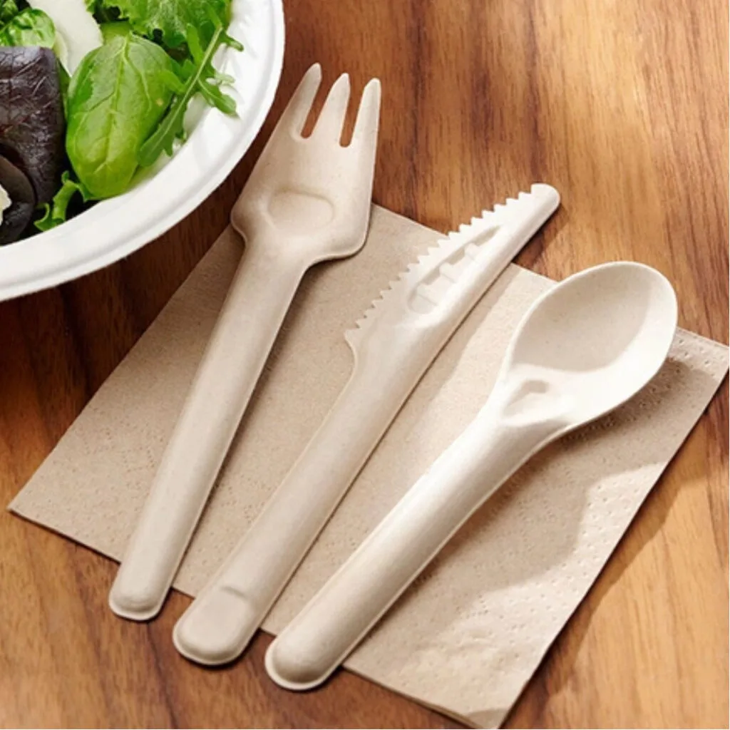 Posate compostabili in bagassa – Utensili ecologici in fibra di canna da zucchero di Bioleader Set di posate compostabili in bagassa realizzato in fibra di canna da zucchero, tra cui forchetta, coltello e cucchiaio, posizionato su un tovagliolo su tavolo di legno, utensili monouso ecologici di Bioleader.