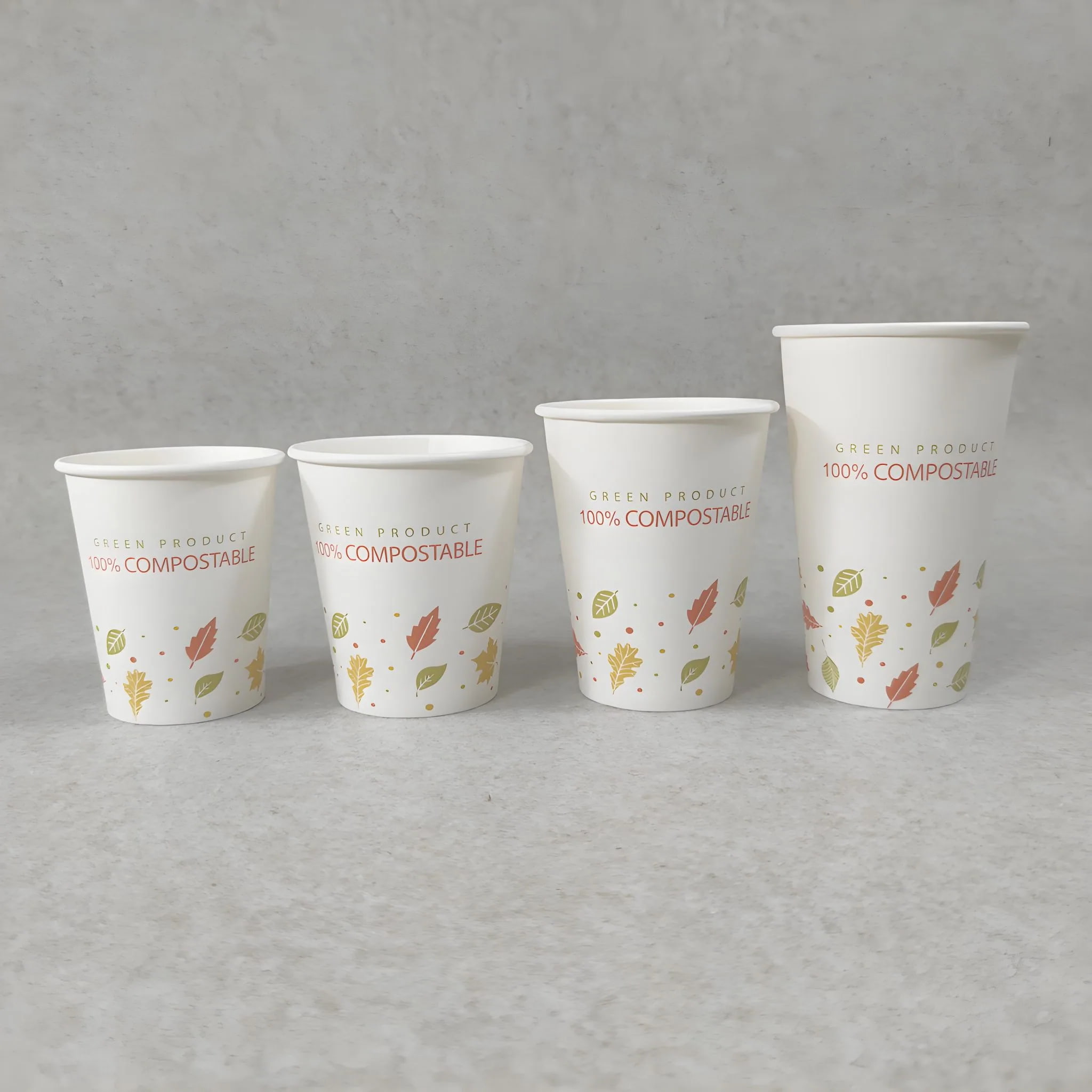 Conjunto de copos de papel compostável com folhas impressas com motivos da natureza e forro em PLA, apresentados em vários tamanhos para bebidas quentes num fundo neutro.