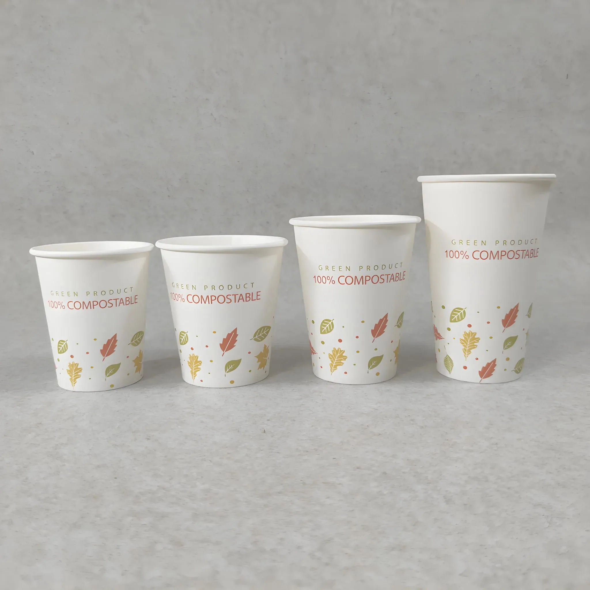 Juego de vasos de papel compostables con hojas impresas en la naturaleza y forro de PLA, presentados en varios tamaños para bebidas calientes sobre un fondo neutro.