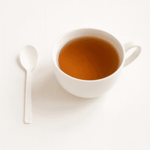 Petite cuillère biodégradable compostable placée à côté d'une tasse de thé sur fond blanc, couverts écologiques pour cafés et vente à emporter