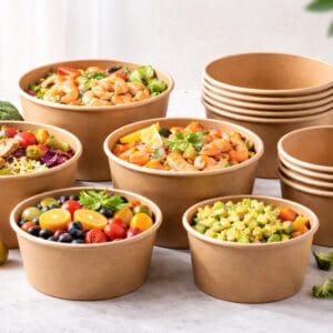Biodegradable PLA-coated paper bowls by Bioleader® in various sizes (6oz to 32oz), filled with vibrant salads, shrimp noodles, and fresh fruit.